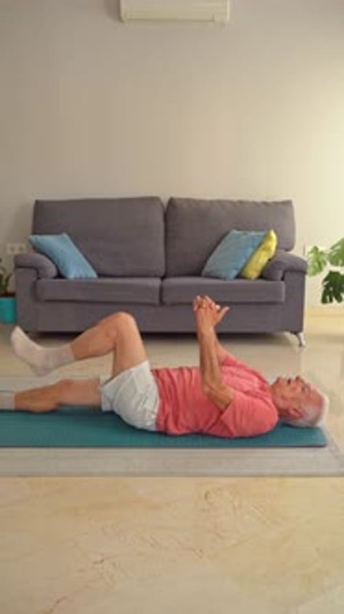Senior Man Stretching Leg on Yoga Mat Indoors