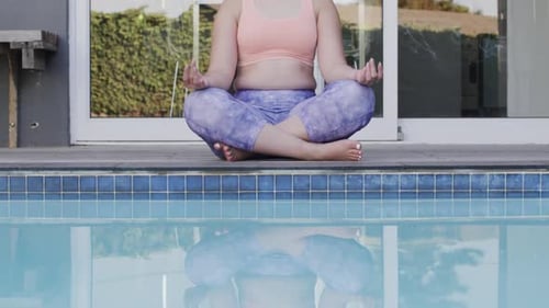 Femme biraciale concentrée pratiquant le yoga et méditant à la piscine dans le jardin Ralenti