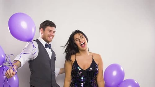 Joyful couple dancing with purple balloons indoors, celebration