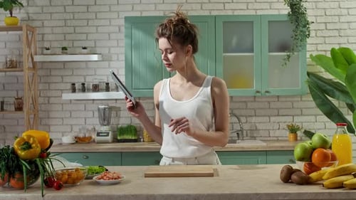 Young Woman at the Table in the Kitchen Preparing Spring Rolls for Healthy Lunch Reading Recipe on