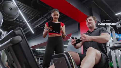 Man Working Out on Rowing Machine with Personal Trainer