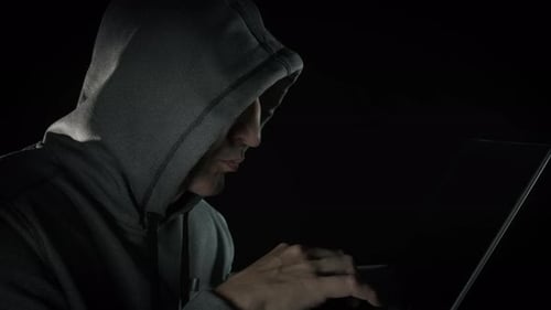 Man in Hoodie Typing on Laptop in Dark