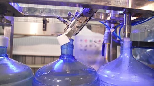 Conveyor belt with big blue flasks moving slowly. Bottles are filled with clean mineral water