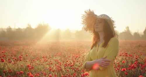 Brunette Woman in a Yellow Dress and Straw Hat in Poppy Field at Sunrise