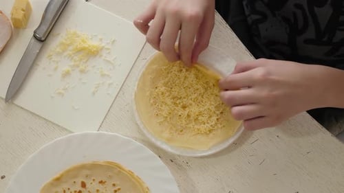 Child Hands Rolling a Pancake with Cheese Filling