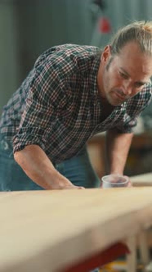Carpenter Applying Varnish with a Roller on a Wood Board