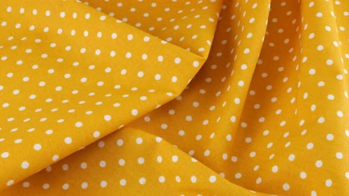Top view of the soft folds of orange yellow with white polka dots cotton fabric rotated
