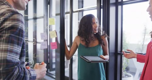 Diversos colegas criativos em discussão, fazendo anotações na parede de vidro no escritório, câmera lenta