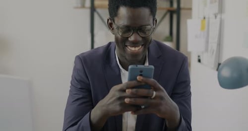 Cheerful African American Businessman Using Smartphone Texting and Smiling in Modern Office