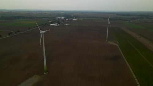 Aerial shot of spinning propeller of wind turbine on agricultural field in the morning.