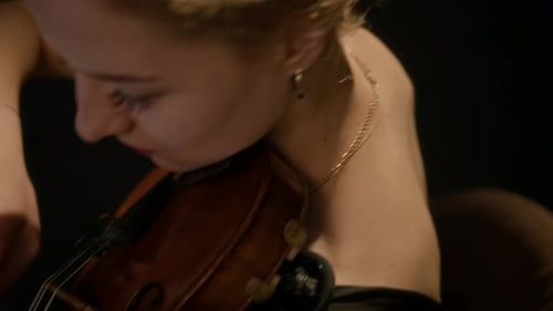 Woman Playing Violin in Dimly Lit Room