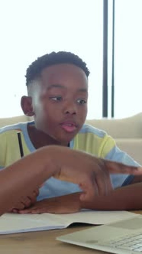 Vertical video: Reading notes striped-tee boy at table asking laptop help with pencil adult guiding