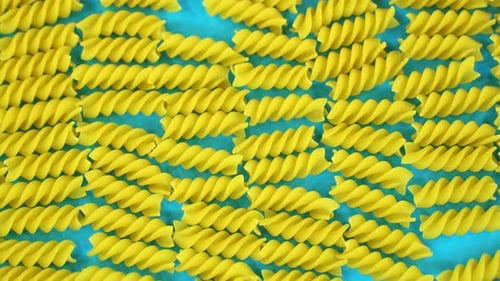 Blick von oben auf ein Set mit rohen Fusilli-Nudeln, die auf blauem Hintergrund geschüttelt werden