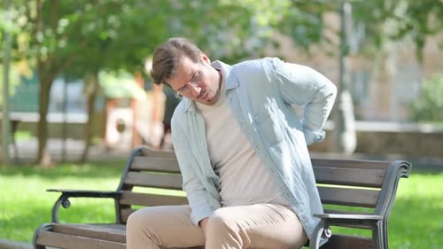 Casual Young Man having Back Pain while Sitting in Park