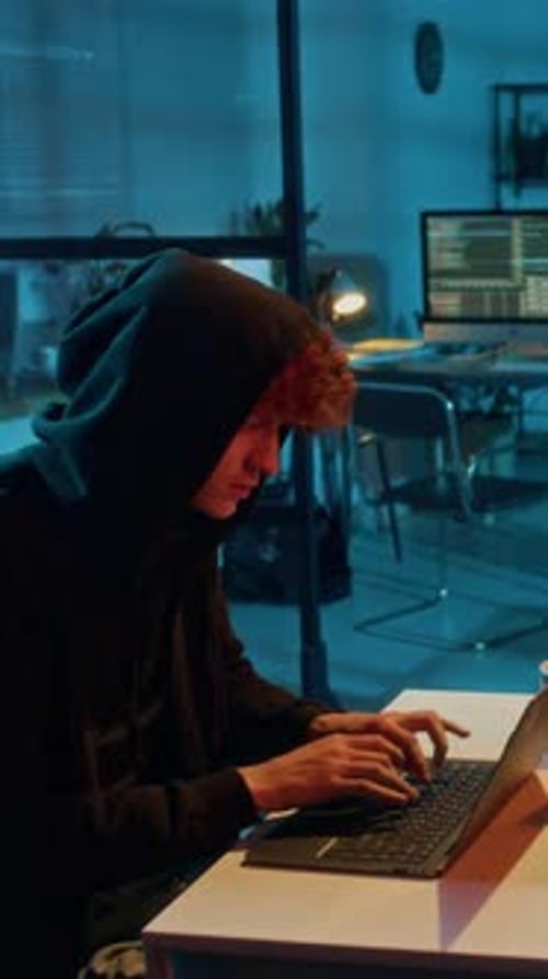 Gen Z Hacker Installing Malicious Drivers on Companys Laptop in Dim Light