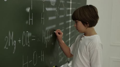 Boy Writes Chemistry Equations on Chalkboard in Classroom
