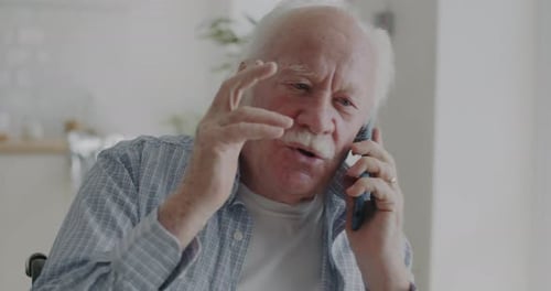 Emotional Elderly Man Speaking on Mobile Phone and Gesturing Indoors in Apartment