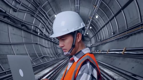 Close Up Side View Of Asian Male Engineer Working On A Laptop In Subway Tunnel
