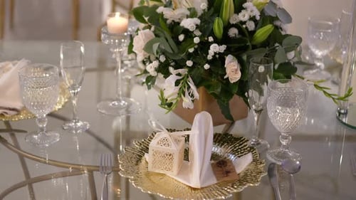 Runder Glastisch, dekoriert mit einem Herzstück aus weißen Rosen und Glasgeschirr. Einzelheiten zur Hochzeit