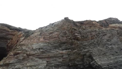 A rugged cliff face with layers of weathered rock formations shot from below on a cloudy day