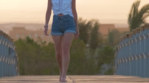 Closeup of Trendy Young Woman Going for a Walk on Long Pier at Seaside with Silhouette of Mountain