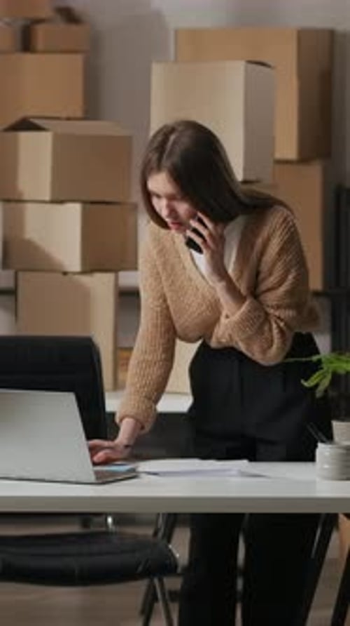 Young Entrepreneur Managing Online Orders in Small Office Workspace Talking on Mobile Phone While