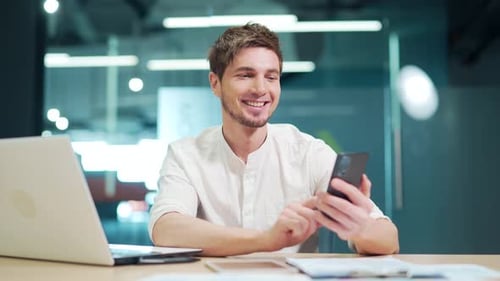 Happy employee using smartphone at work in modern office. Satisfied caucasian manager using a mobile
