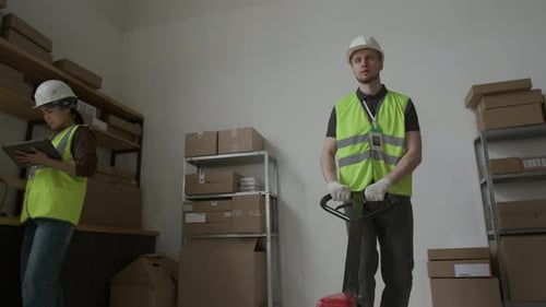 Male Employee Moving Heavy Loads with Pallet Truck and Giving Coworker Nod