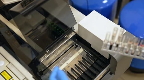 Gloved hand of a laboratory expert puts the stand with test tubes into equipment.