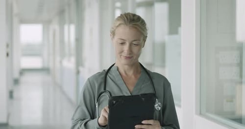 Mature Female Doctor standing in modern hospital corridor working on digital tablet