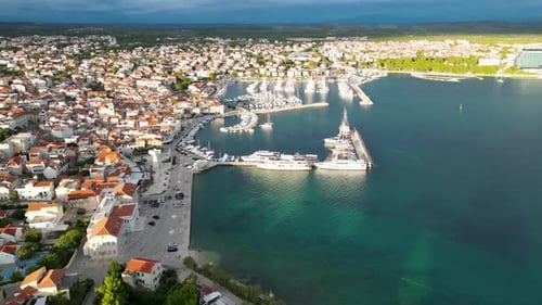 Drone flying forward, parallel to a small croatian city. The camera is panning down to a harbour fil
