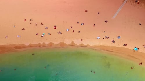 Tranquil waves arrive slowly to the lovely sandy beach. Vacationers rest at the shore sunbathing.