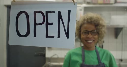 Sign That Says Open in a Restaurant with an Owner or Waitress in the Background Out of Focus