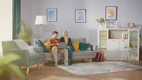 Couple relaxing on couch using laptop together at home