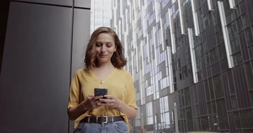 Pretty adult female using smart phone outside modern office building