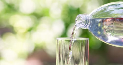 Reines Wasser, das aus einer Flasche auf grünem Naturhintergrund in Glas gegossen wird