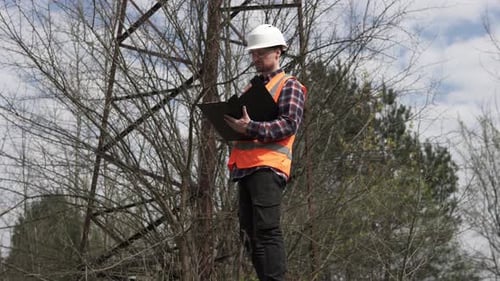 Engineer Inspecting Electrical Tower Infrastructure in Nature