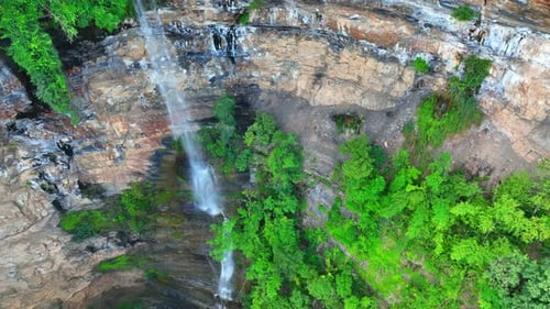 Forest waterfall cascades from cliff, captured by drone.