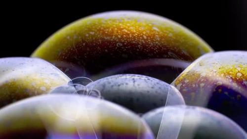 Close-up image of soap bubbles on a black background, golden iridescent surfaces. Slow motion