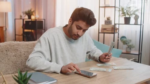Man Counts Money and Uses Phone at Table