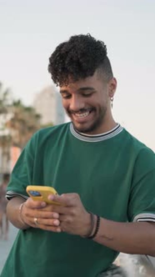 Young Afro Man Smiling While Using His Mobile Phone Outdoors on the Street During Sunset