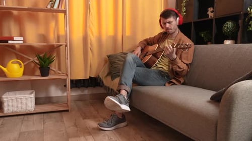 Man Playing Guitar on Couch With Headphones