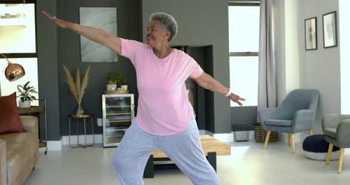 Mulher afro-americana sênior adotando uma postura ampla, estendendo os braços, melhorando o equilíbrio em casa