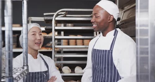 Portrait of happy diverse bakers in bakery kitchen with arms crossed in slow motion