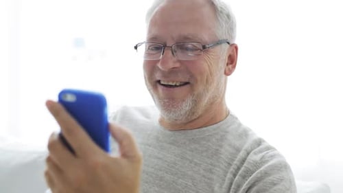 Senior man smiling using mobile phone at home