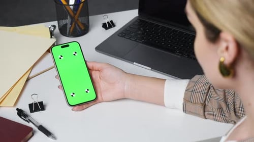 Woman holds smartphone with green screen in office