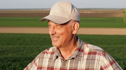 Close up portrait of senior farmer standing in field at sunset looking at distance.