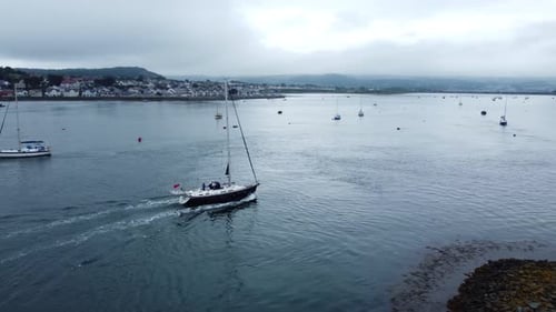 Sailing boat aerial view navigating quiet river Conwy seaside town harbour estuary
