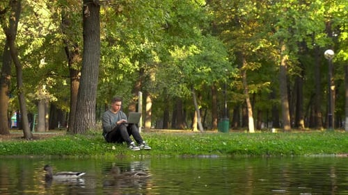 Young Man Working on Laptop in Riverside Park