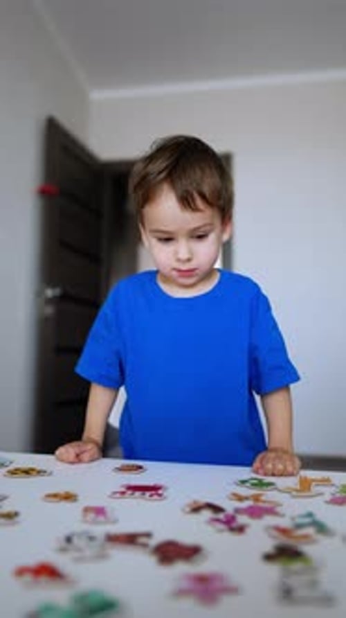 Smart cute toddler kid looks at the puzzles scattered on the desk in front of him.